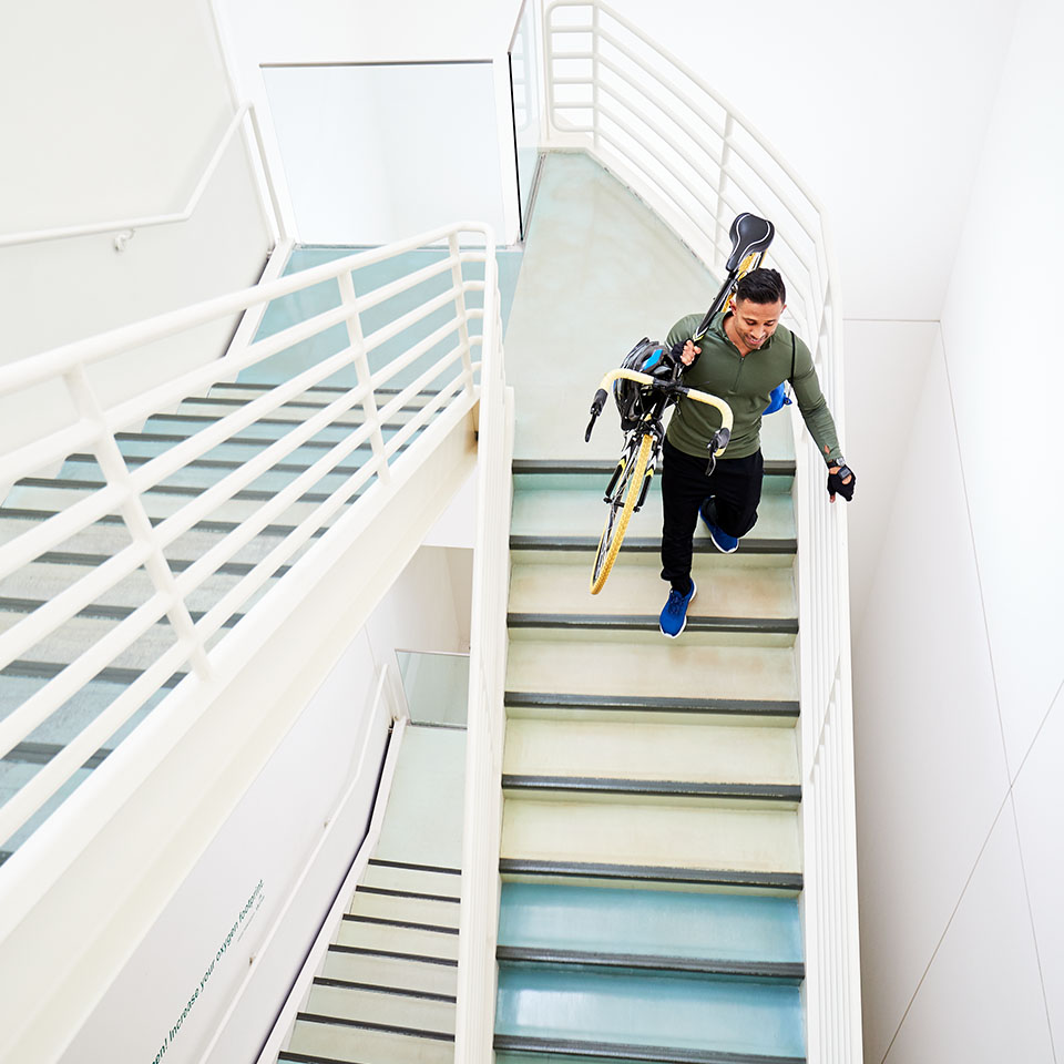 A young man carries a bicycle down a stairwell.